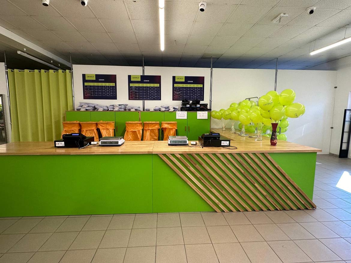 dlouhý zelený prodejní pult, zelené skříňky a oranžové vysoké odpadkové koše v pozadí